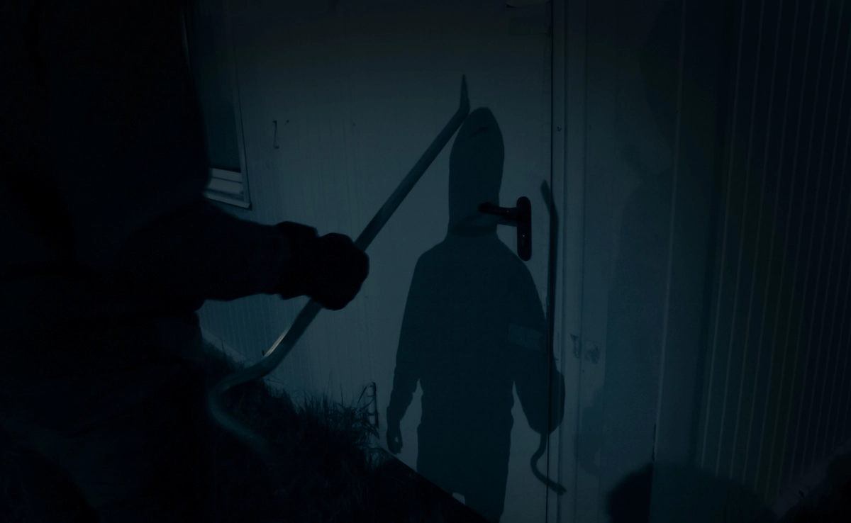 Schatten eines Einbrechers mit Brecheisen an Tür in der Nacht