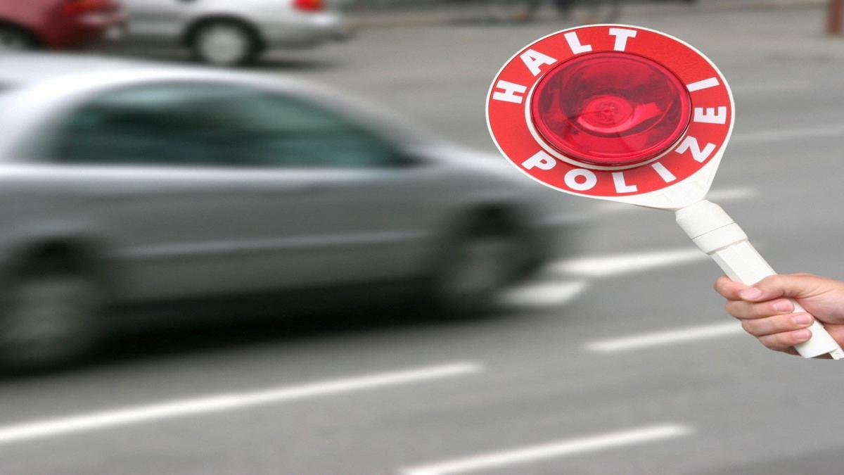 Polizeikelle mit „Halt“-Signal vor vorbeifahrendem Auto in der Schweiz