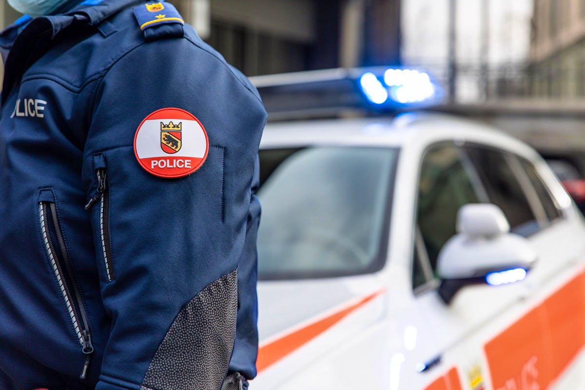 Polizist in Uniform der Kantonspolizei Bern steht vor einem Polizeiauto mit Blaulicht