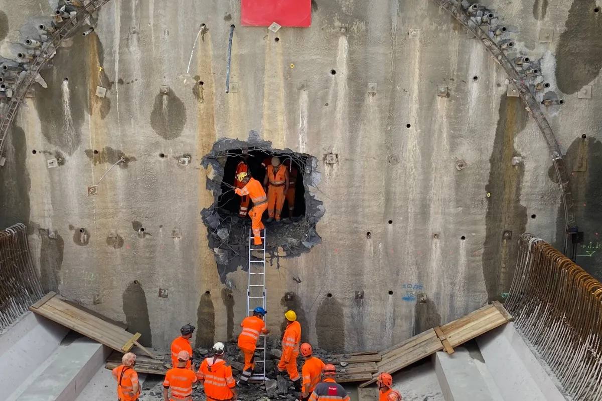 Tunnelwand mit Durchbruchöffnung und Bauarbeitern auf Leiter bei der Durchschlagfeier