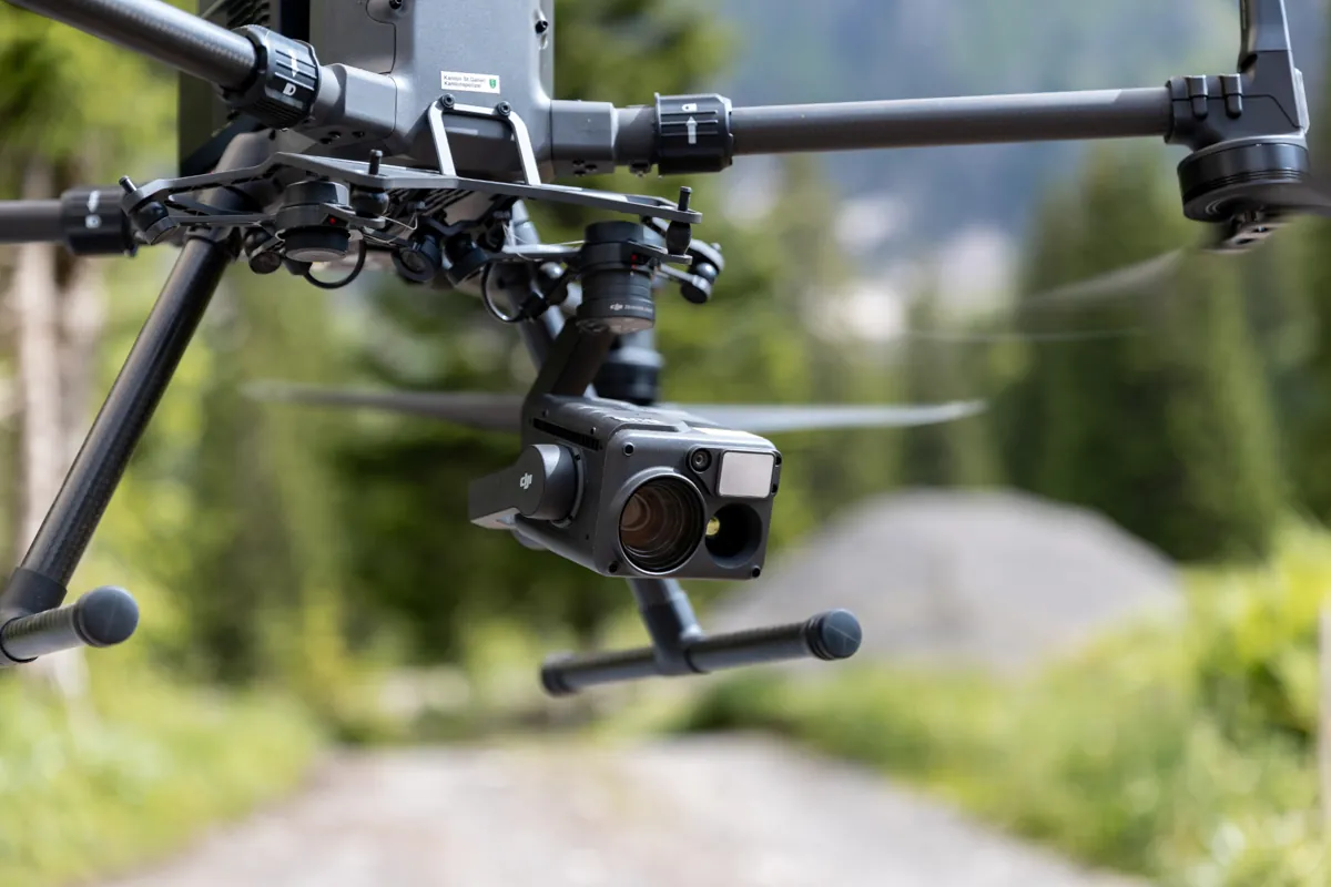 Nahaufnahme einer professionellen Drohne mit Kamera im Einsatz über einem Waldweg in der Schweiz