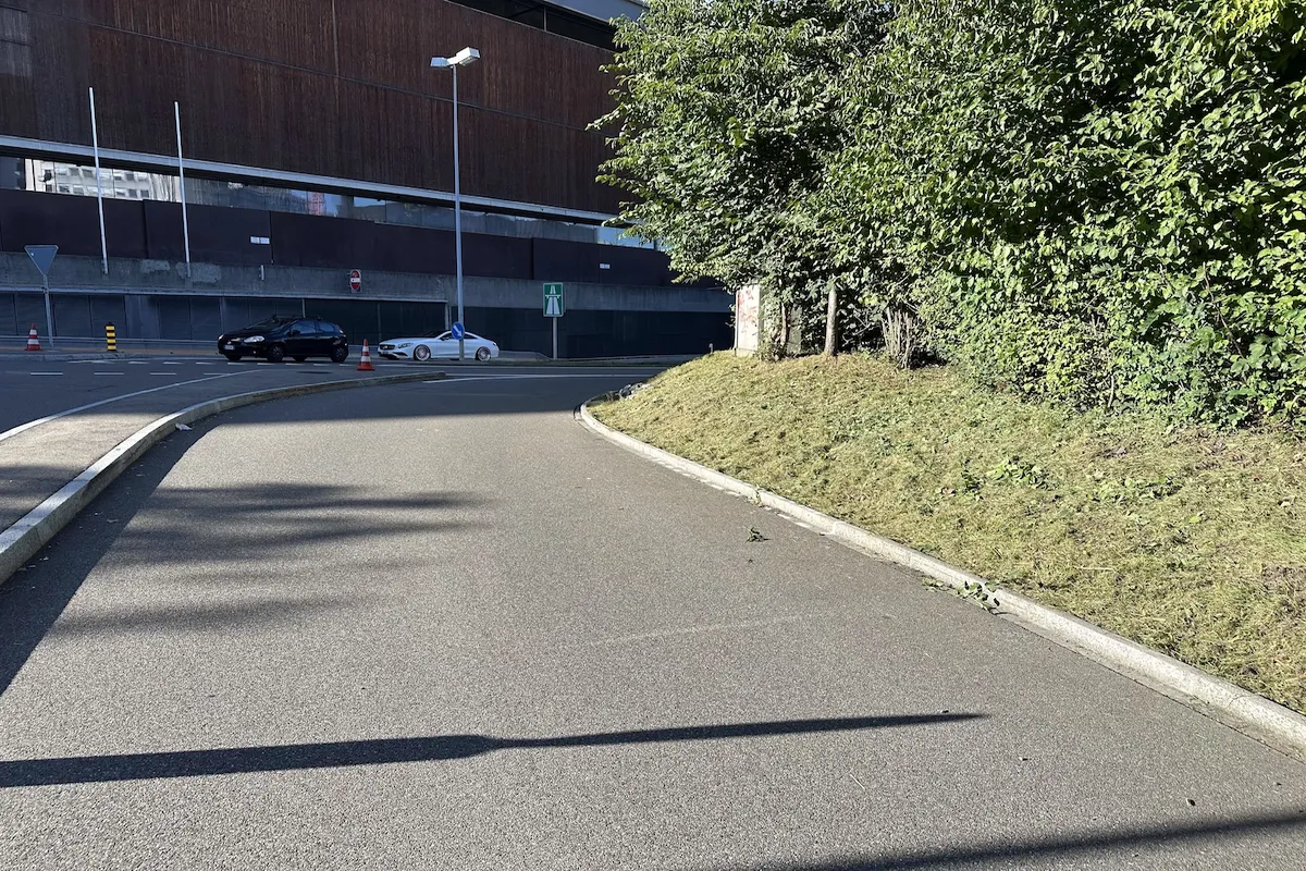 Asphaltierte Einmündung mit Randstein, Absperrkegel und zwei Autos im Hintergrund